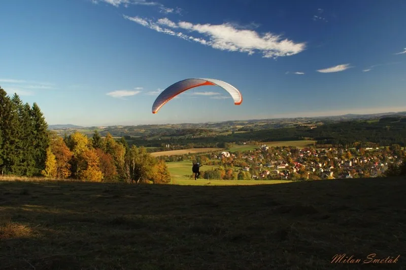 Paraglidista nad podzimní krajinou u Plav